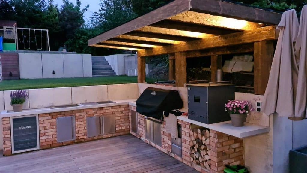 Gartenküche aus rustikalen Holzbalken mit Beleuchtung